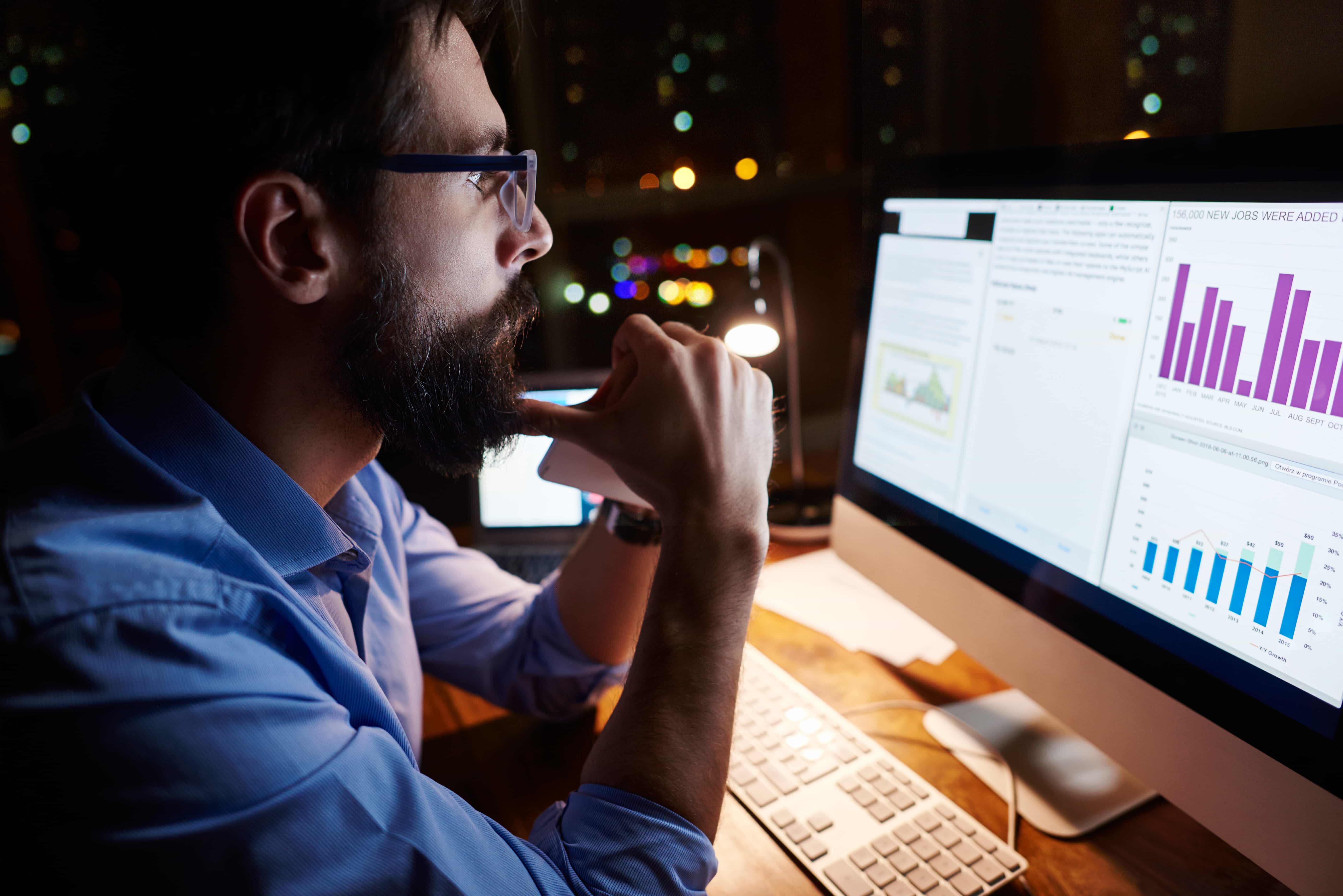 A young businessman with a beard and glasses analyzing seasonal systems engineering metrics on a computer monitor in Seattle, WA. A young businessman with a beard and glasses analyzing seasonal systems engineering metrics on a computer monitor in Seattle, WA.
