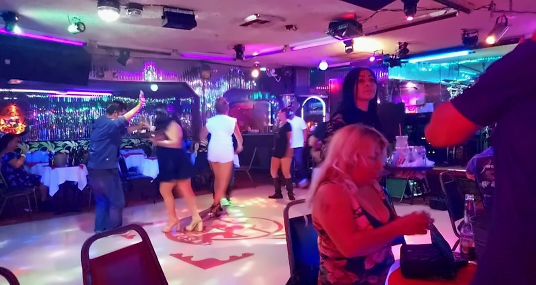 Couples dancing on the lit dance floor at La Zona Rosa with the bar and tables behind them