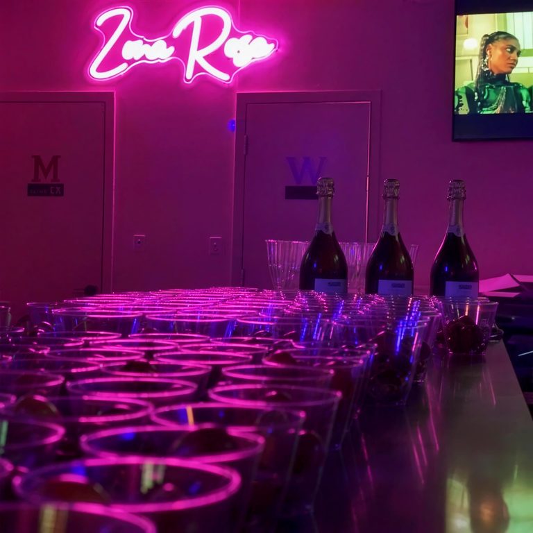 A table set with glasses and bottles beneath the pink 'Zona Rosa' neon sign