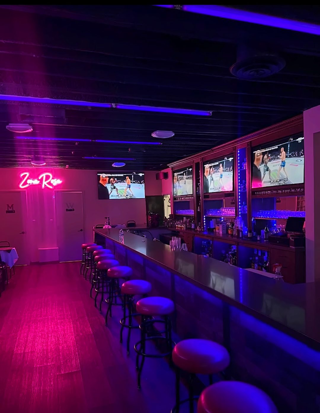 The long bar at La Zona Rosa under pink and blue light with the neon sign glowing on the far wall
