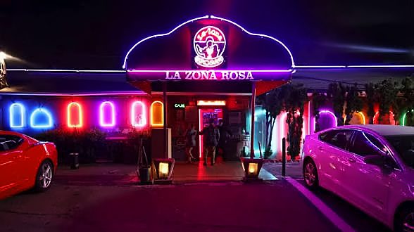 Cars parked in front of La Zona Rosa's neon-lit entrance at night