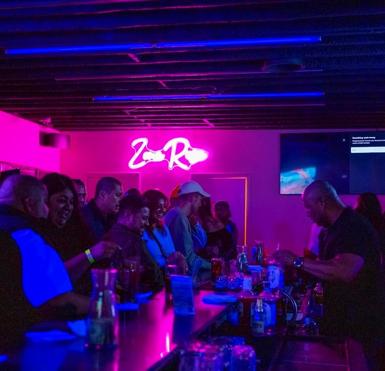 Guests gathered along the bar beneath the pink neon sign