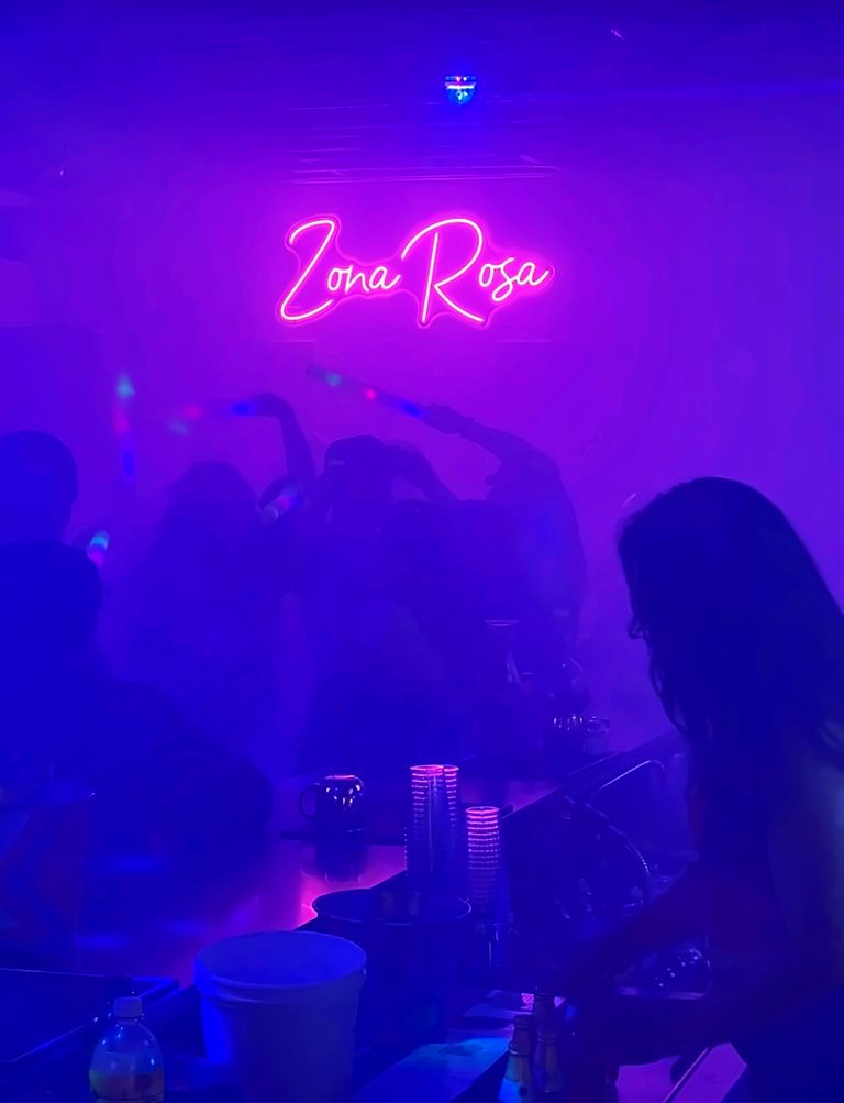 A crowd in violet haze beneath the neon sign on a packed night