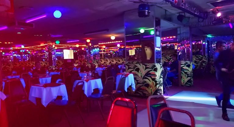 The main room at La Zona Rosa with white-clothed tables around the dance floor under colored lights