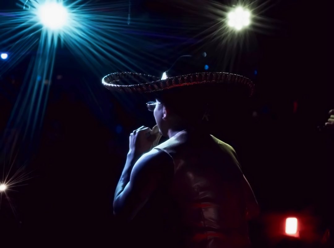 A singer in a wide-brimmed hat silhouetted against stage lights at La Zona Rosa
