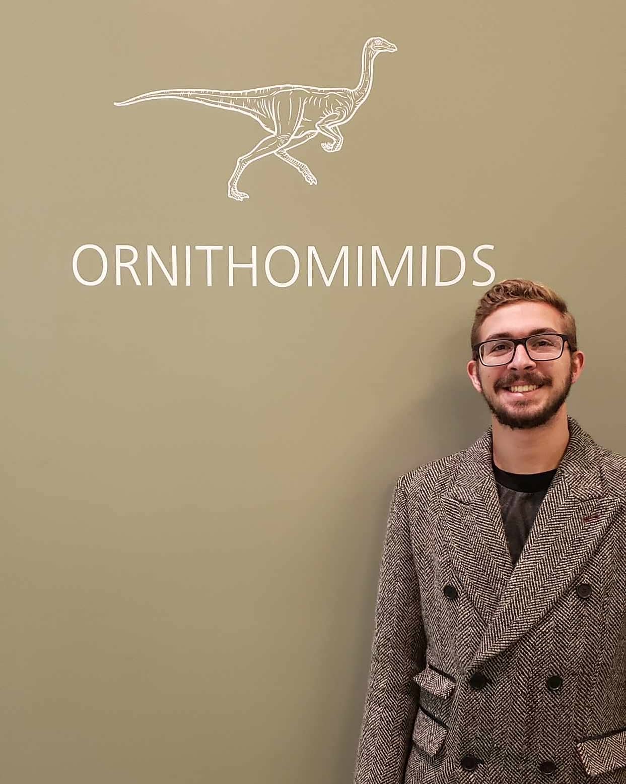 Evan Jevnikar as an adult paleontologist at the same dinosaur museum exhibit.