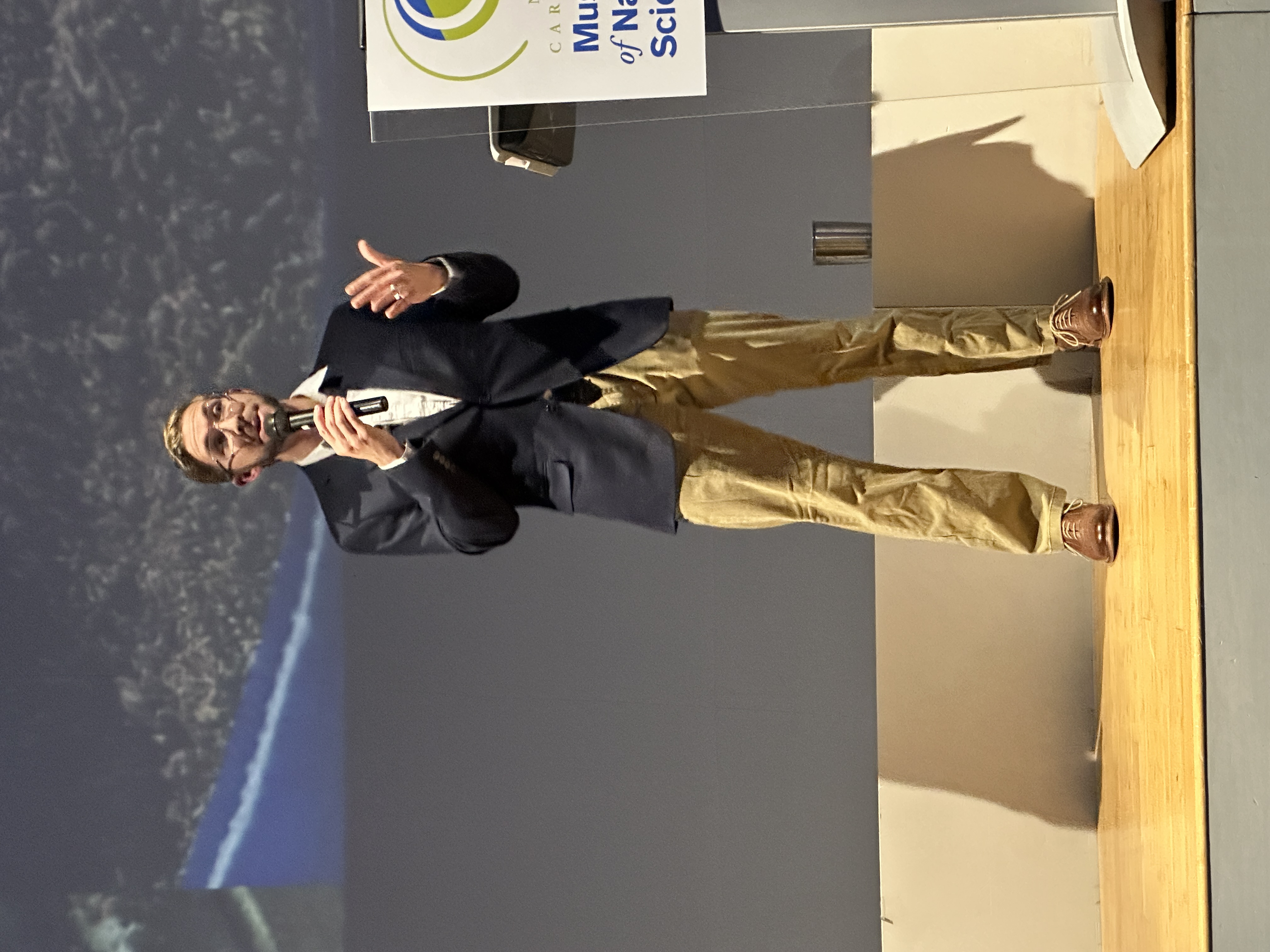 Stage portrait, Evan Jevnikar speaking at the North Carolina Museum of Natural Sciences.