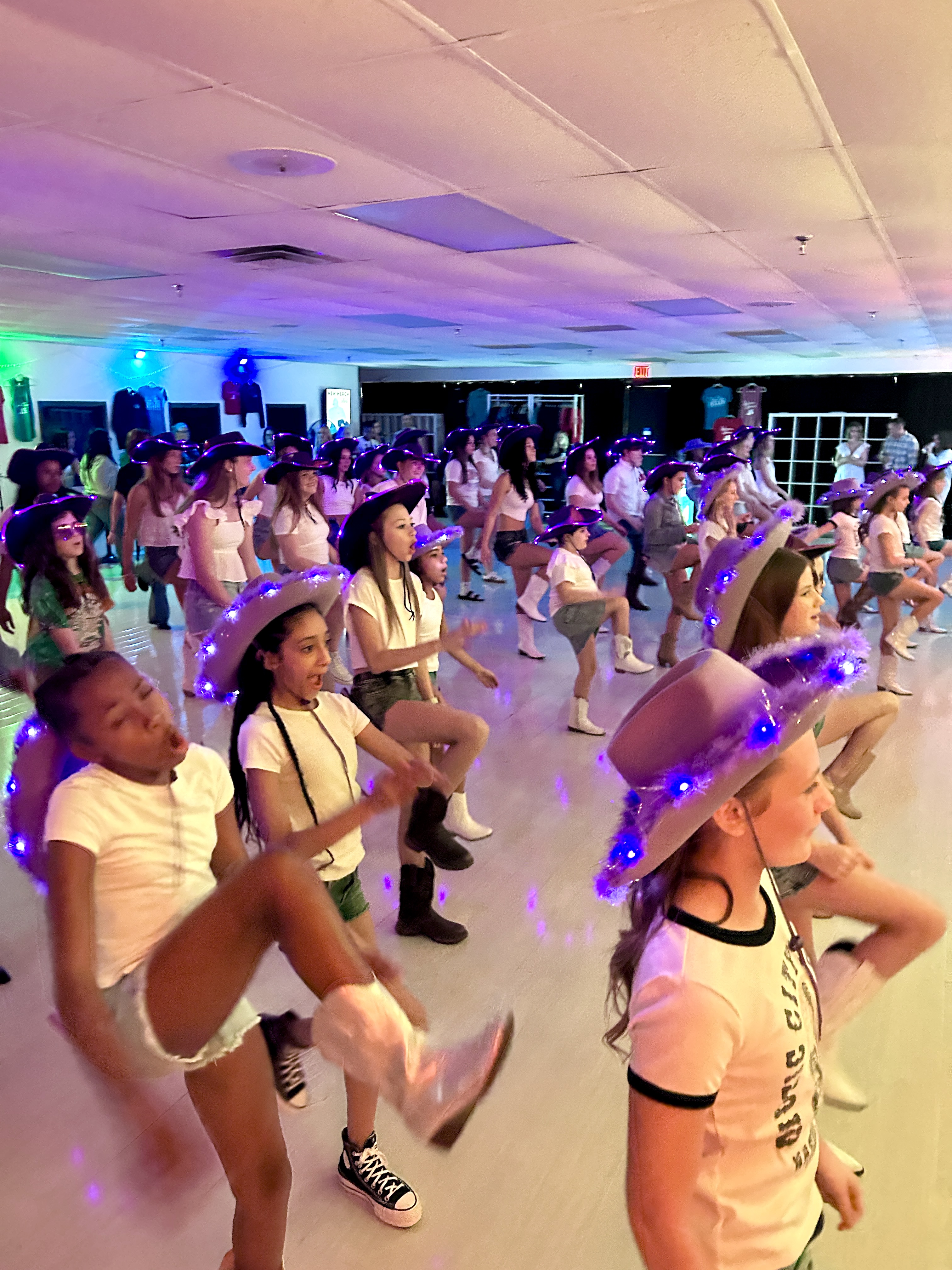 Kids dancing and kicking in light-up cowboy hats at the studio.