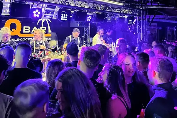 Gäste vor dem beleuchteten Cocktailanhänger mit Barkeepern