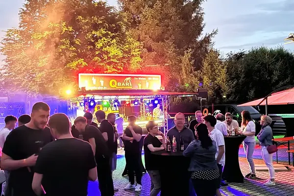 Gäste an Stehtischen vor dem Cocktailanhänger auf einem Firmenfest