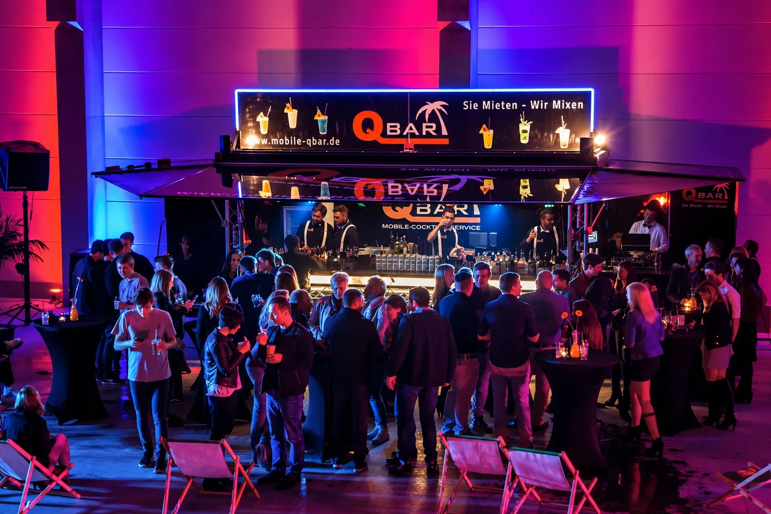 Mitarbeiterevent in einer Halle: Gäste an Stehtischen vor dem beleuchteten QBAR Cocktailanhänger