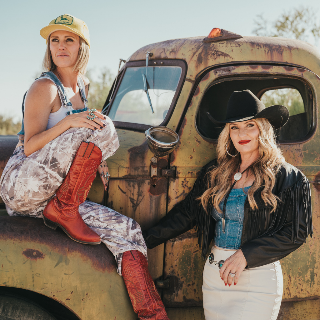 Gretchen and Missy sitting on the hood of a vintage rusty truck wearing denim and cowboy boots.