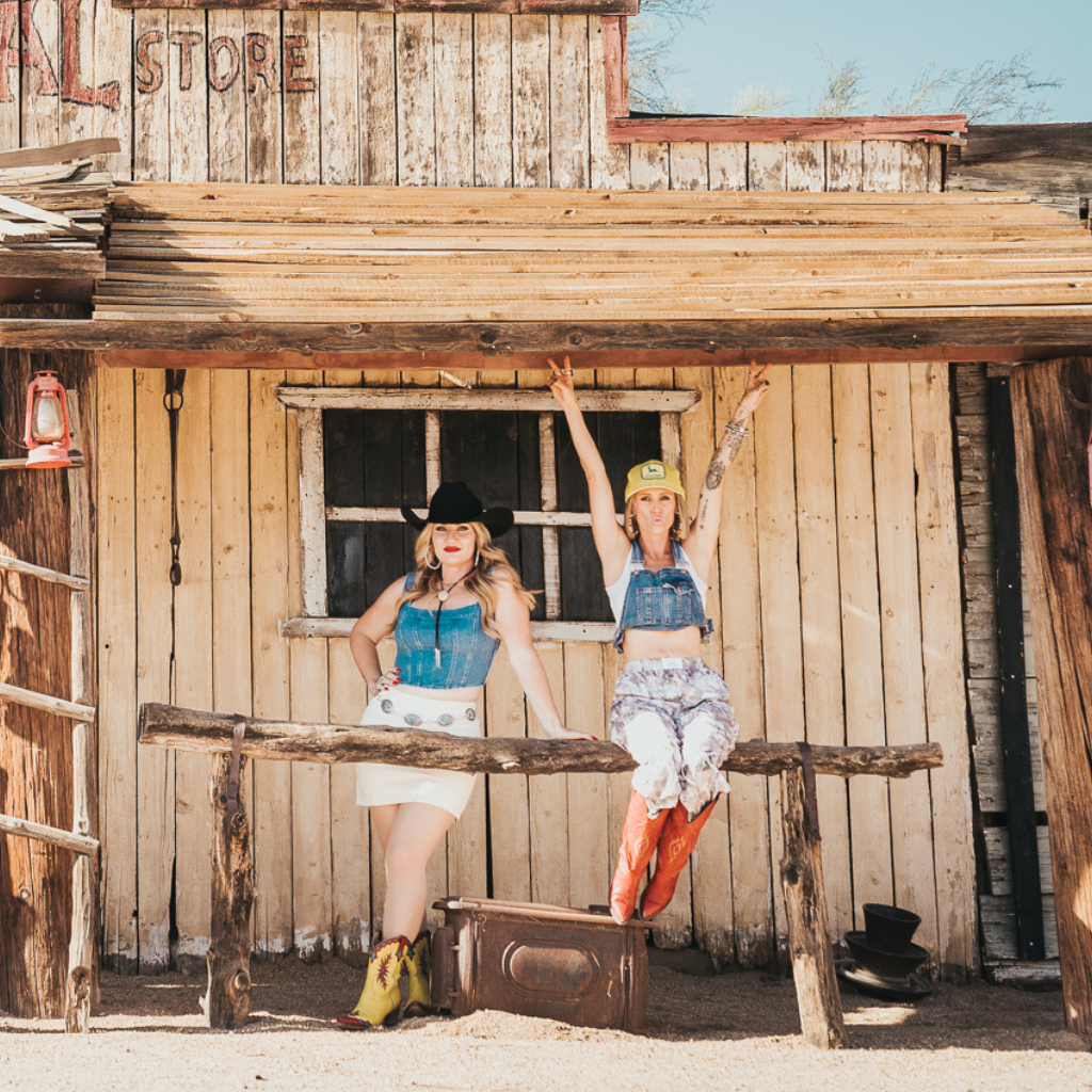Gretchen and Missy posing in front of a rustic, weathered wooden "nut farm" shack in the desert.