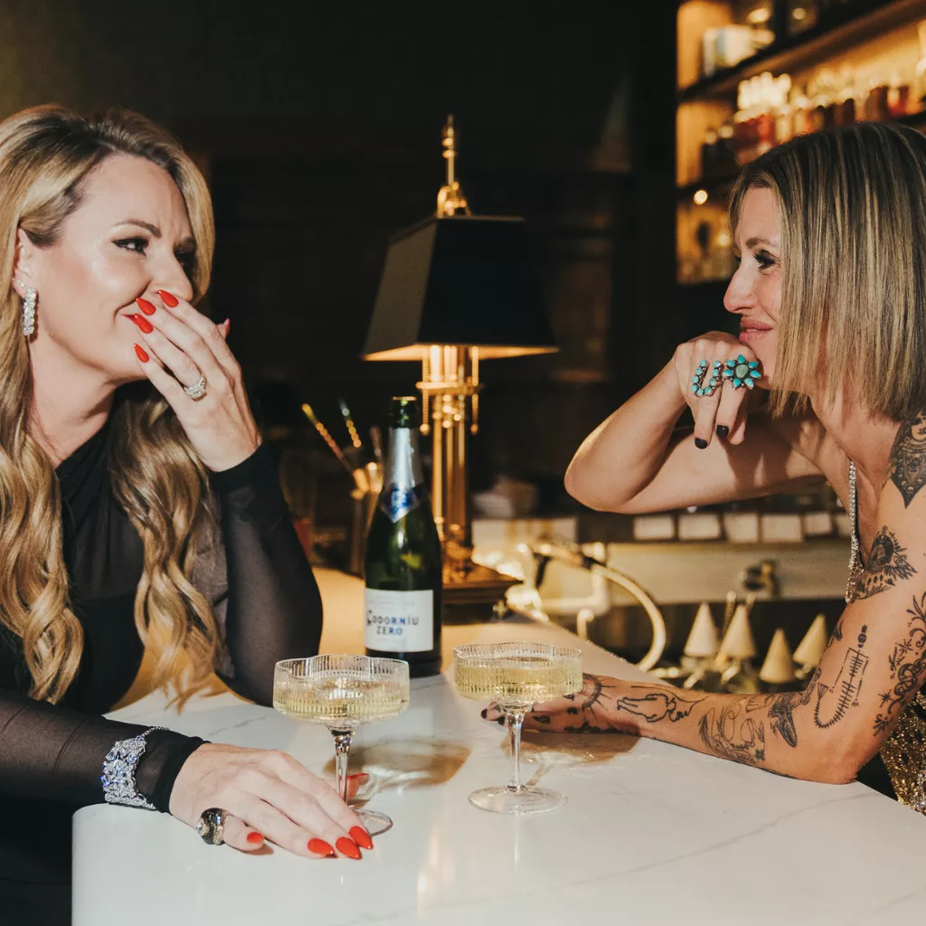 Gretchen and Missy sharing a non-alcoholic drink at a bar while recording or discussing an episode of The Nut Farm.