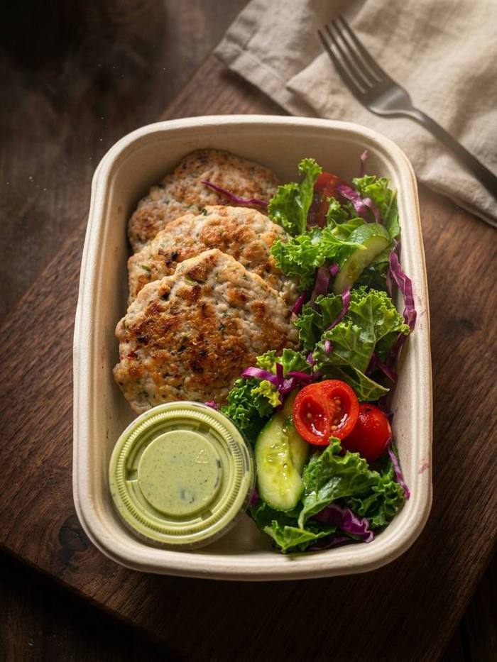Balanced meal box with herbed patties, salad and dressing