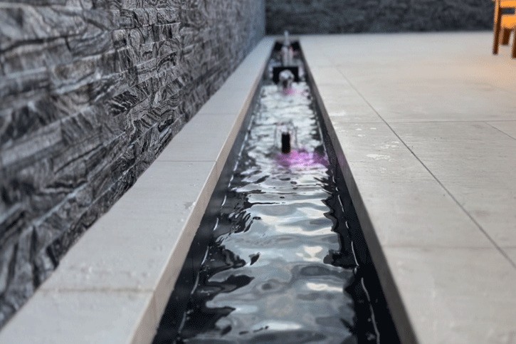 Close-up of the narrow waterway channel with bubblers between a stacked stone wall and limestone paving