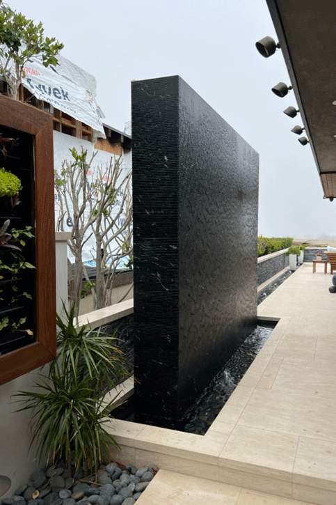 Black tile water wall under construction in Corona del Mar, rising out of the perimeter waterway beside an ipe-framed living wall panel