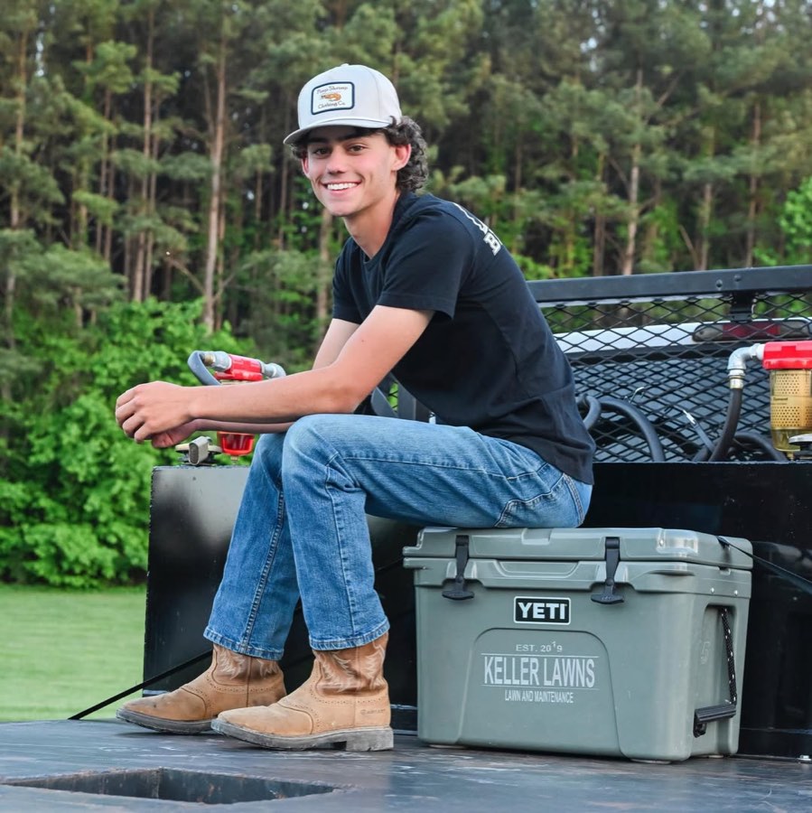 Carson Keller, owner of Keller Lawns, sitting on his work truck with a Keller Lawns cooler