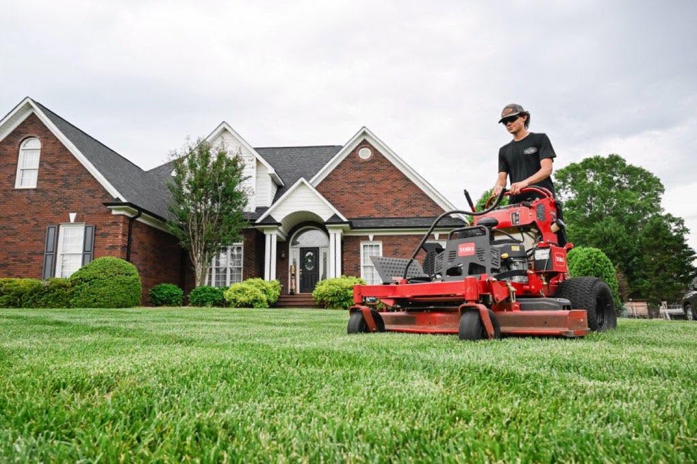 Carson Keller mowing clean stripes into a lawn in front of a brick home in Harrisburg, North Carolina