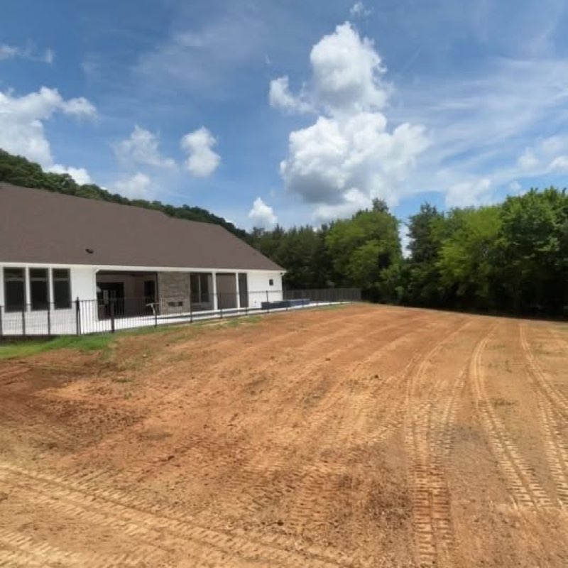 Freshly graded red-clay building pad beside a home, leveled with a skid steer by Keller Lawns in Cabarrus County, NC