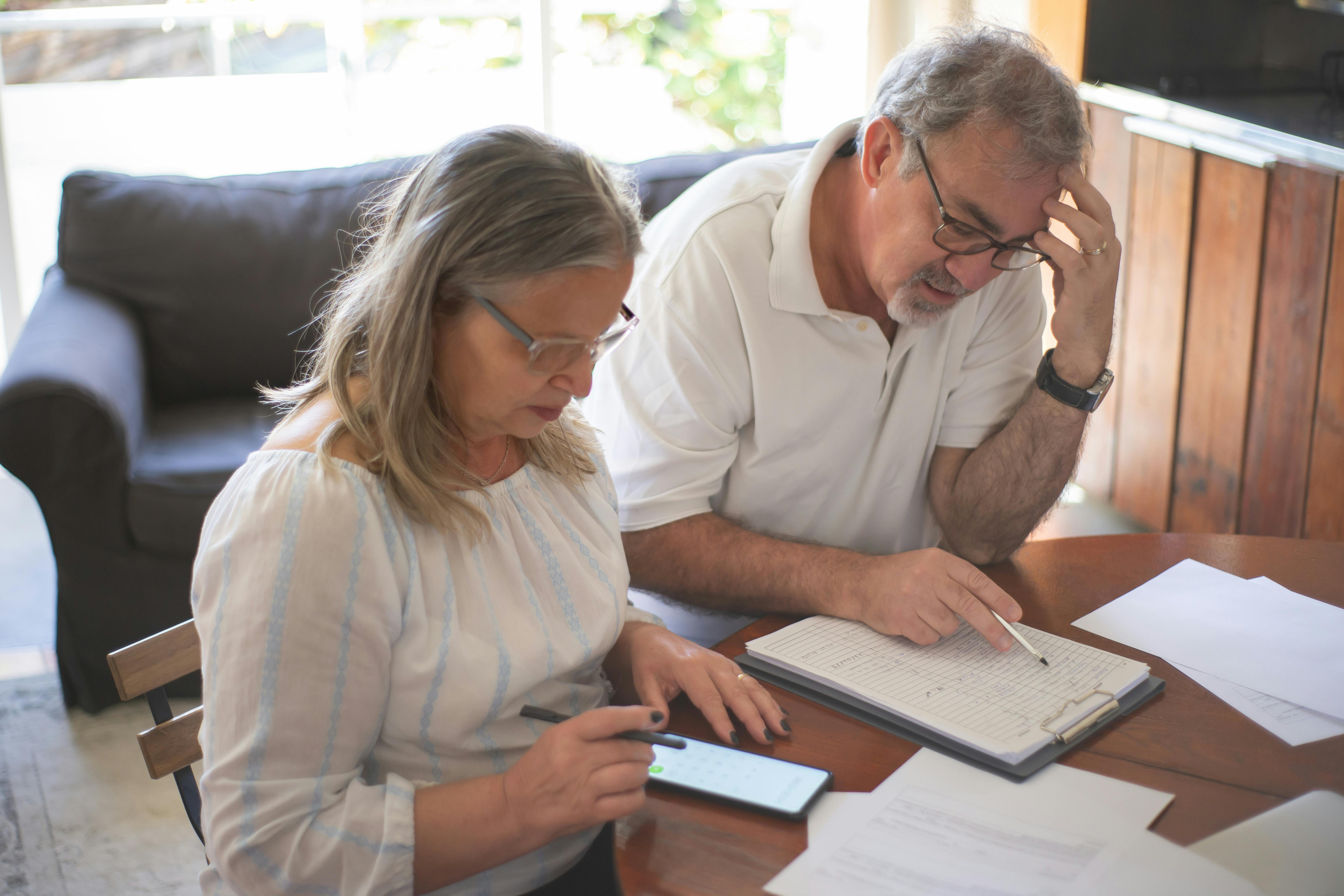 Senior homeowners reviewing rising property tax bills in a paid-off home. Senior homeowners reviewing rising property tax bills in a paid-off home.