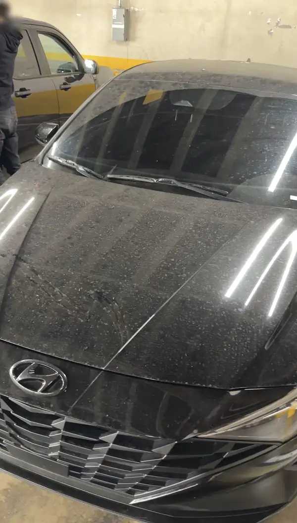 Front of a black Hyundai Elantra coated in dust in a parking garage, before a wash