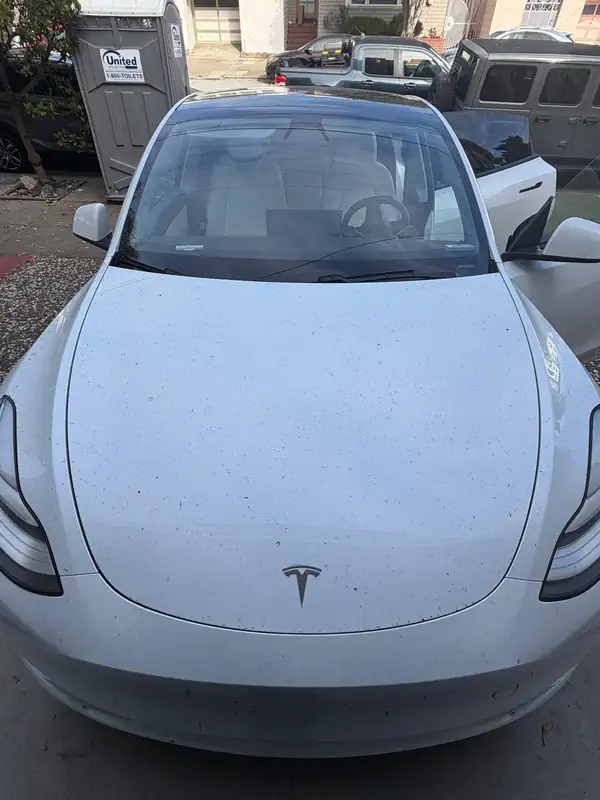 Front of a white Tesla Model Y before detailing, with black specks across the hood and a dusty windshield