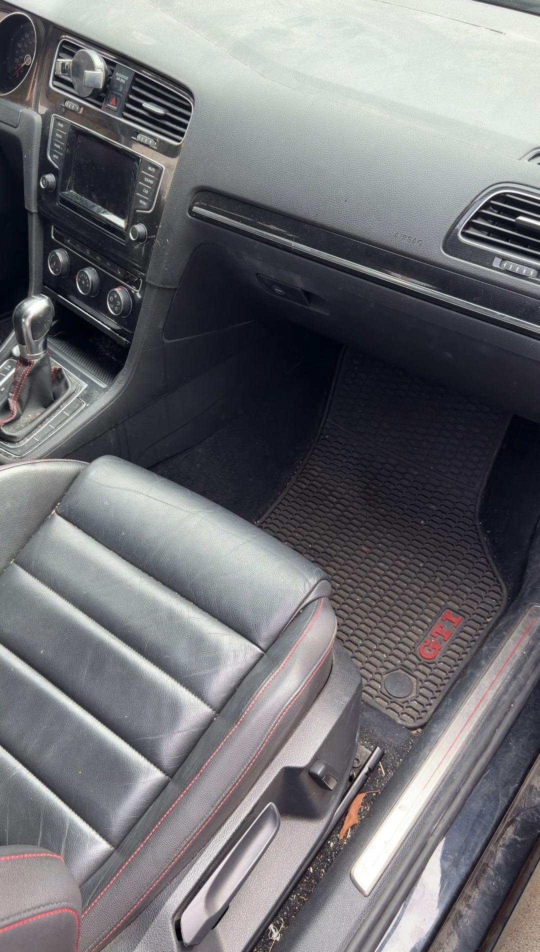 Passenger footwell and dash of a black VW GTI before cleaning, dust on the dash