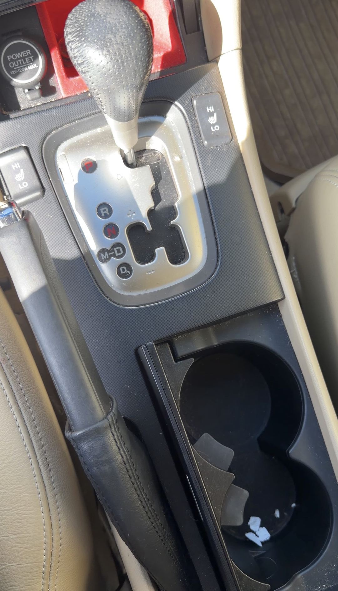 Automatic shifter, seat-heater switches and cupholders of an Acura sedan before detailing, with dust on the console and paper fragments in a cupholder.