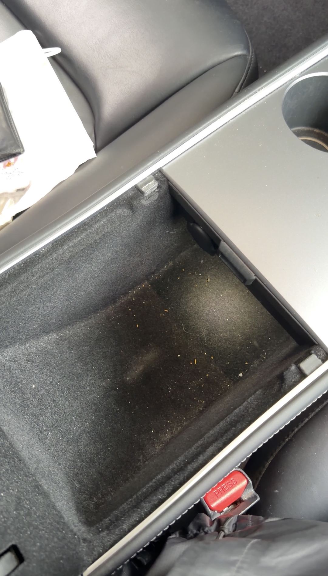 Close-up of a Tesla Model 3 console storage bin before cleaning, crumbs and fibres in the lining