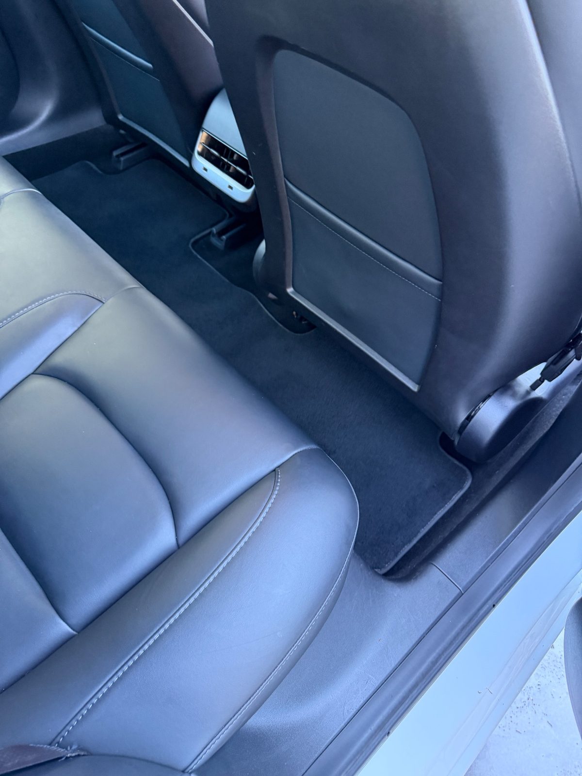 Rear footwell of a white Tesla Model 3 after detailing, with clean carpet