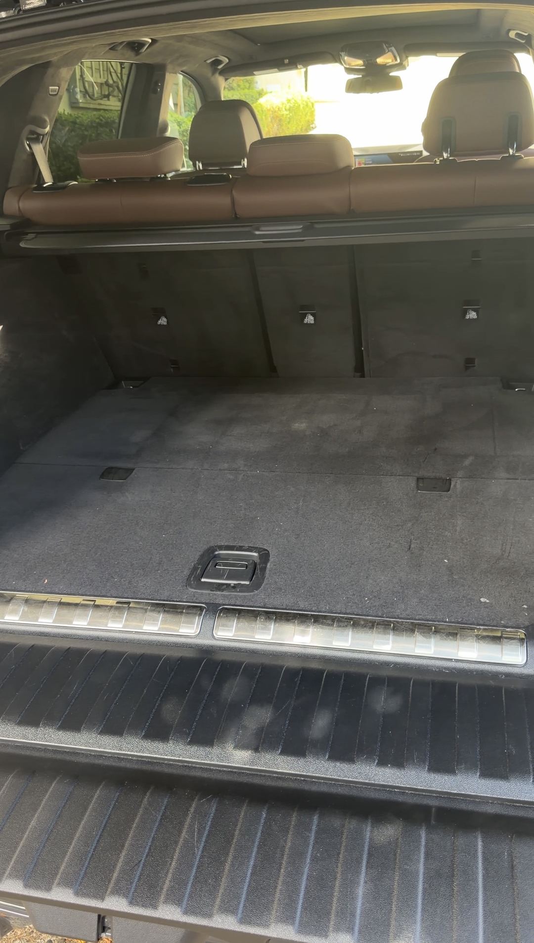 Cargo bay of a BMW X5 before detailing, with matted carpet and grimy chrome sill trims