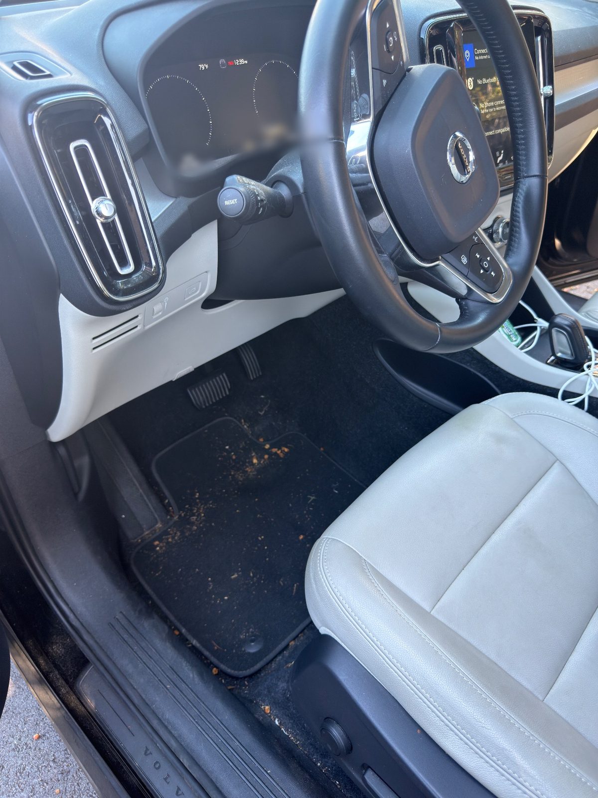 Driver footwell of a Volvo XC40 before detailing, with crumbs and debris scattered across the black mat