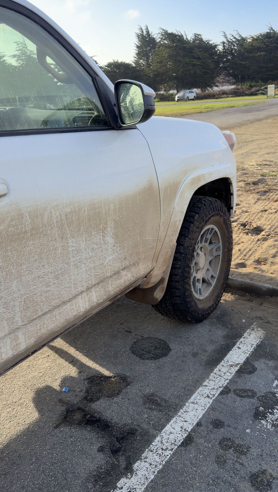 Dusty front passenger door and dust-coated wheel of a white Toyota 4Runner parked by a sandy lot