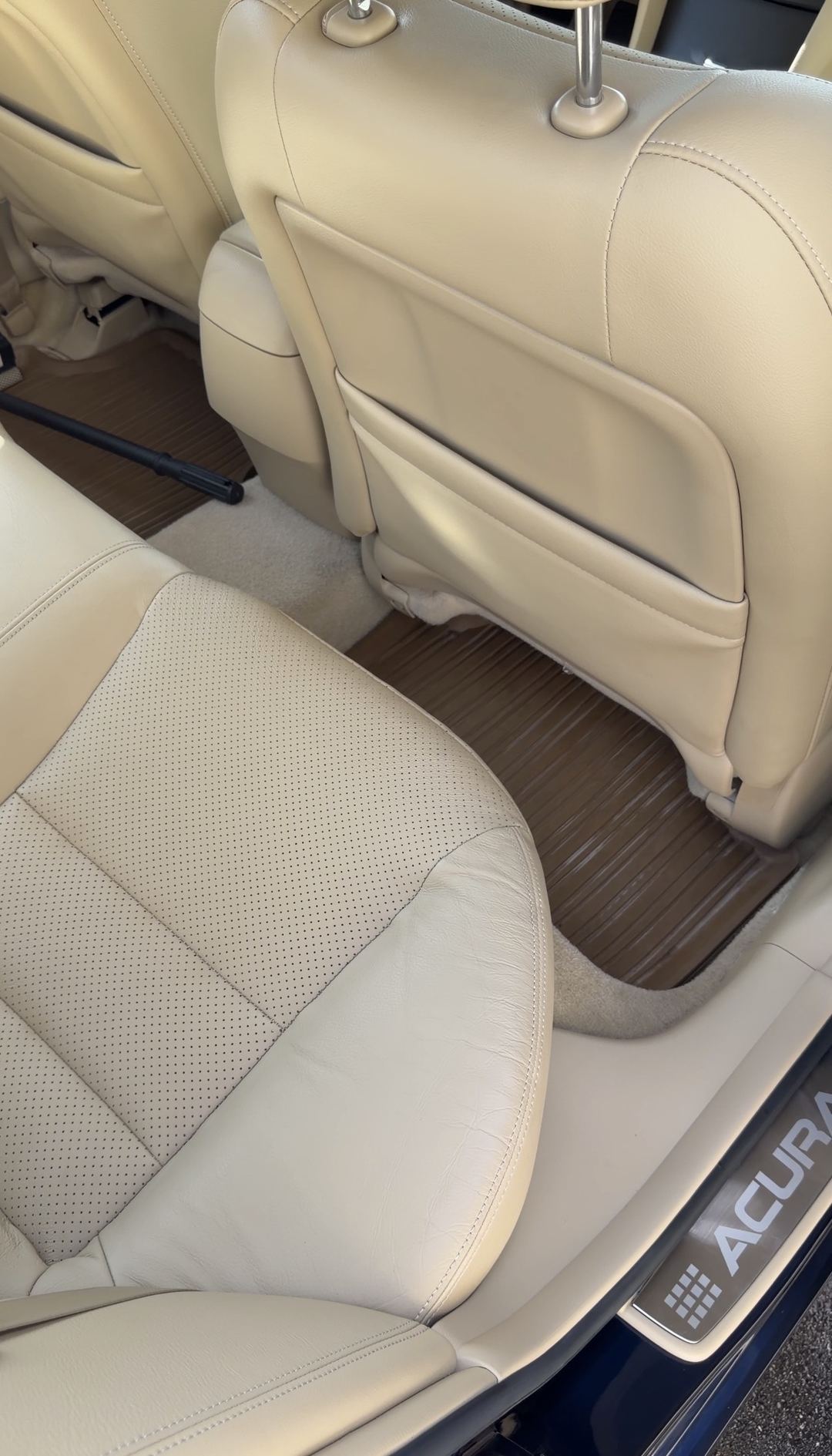 Cleaned rear passenger-side footwell of an Acura sedan after detailing, with a detailer's vacuum wand resting in the opposite footwell.