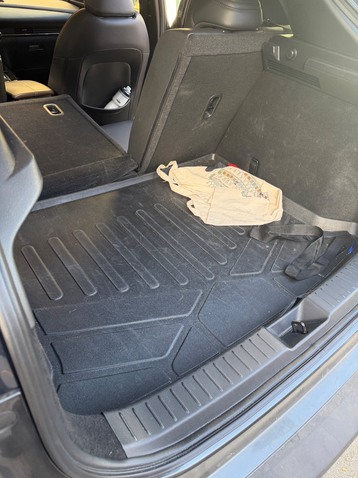 Cargo area of a grey Mazda CX-30 before detailing with dusty liner and a tote bag