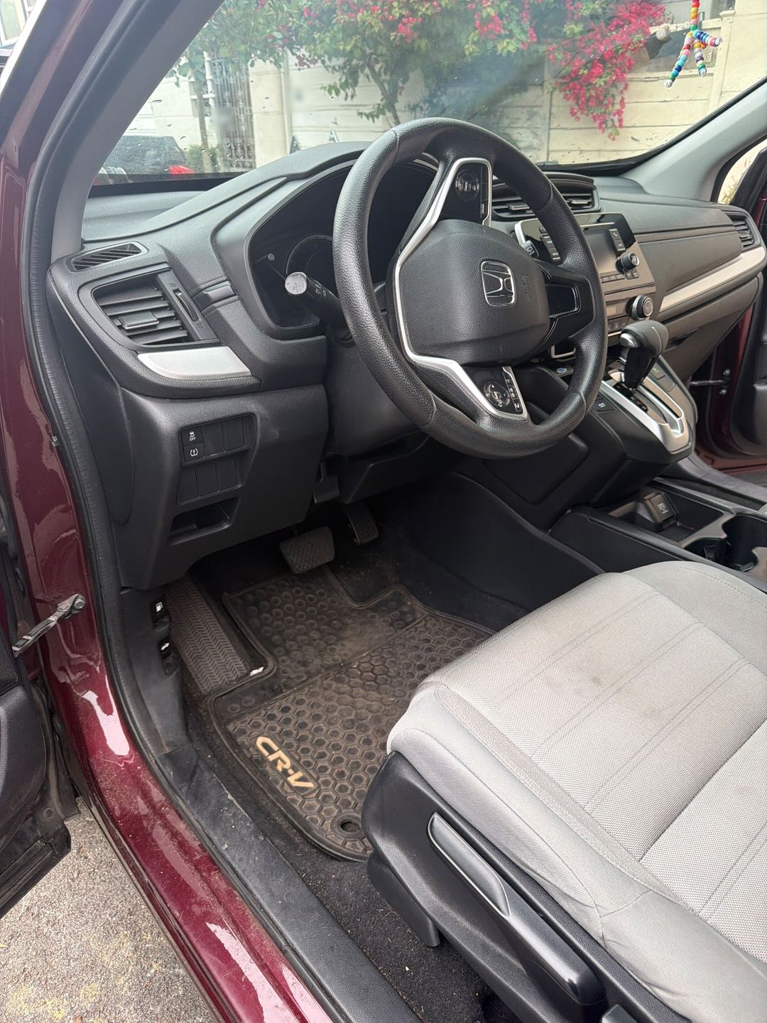 Driver footwell of a maroon Honda CR-V before detailing, the rubber floor mat grey with dust and grit