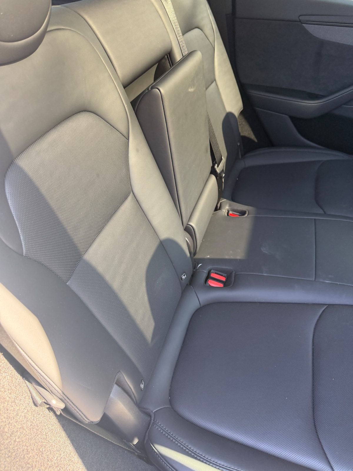Rear seat of a white Tesla Model Y before cleaning, dusty dull leather