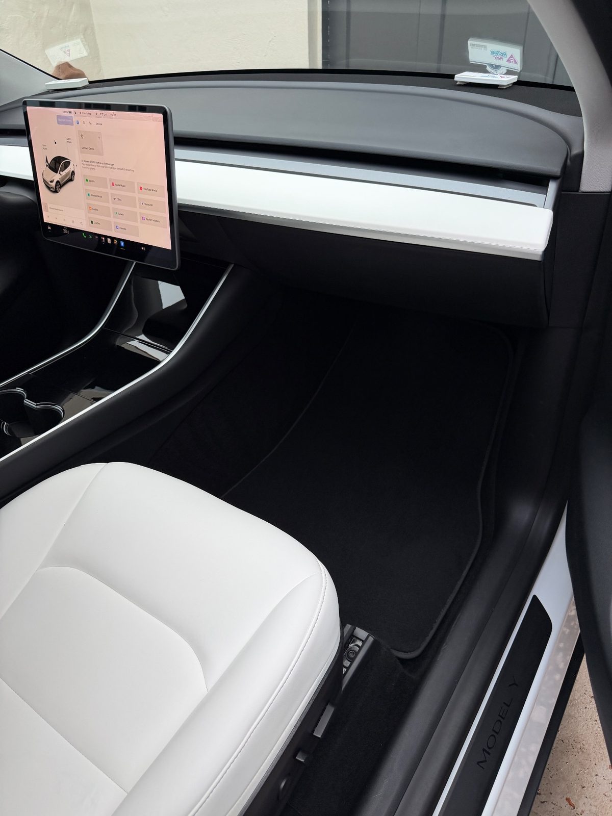 Passenger footwell and dash of a white Tesla Model Y after detailing, with a clean carpet mat