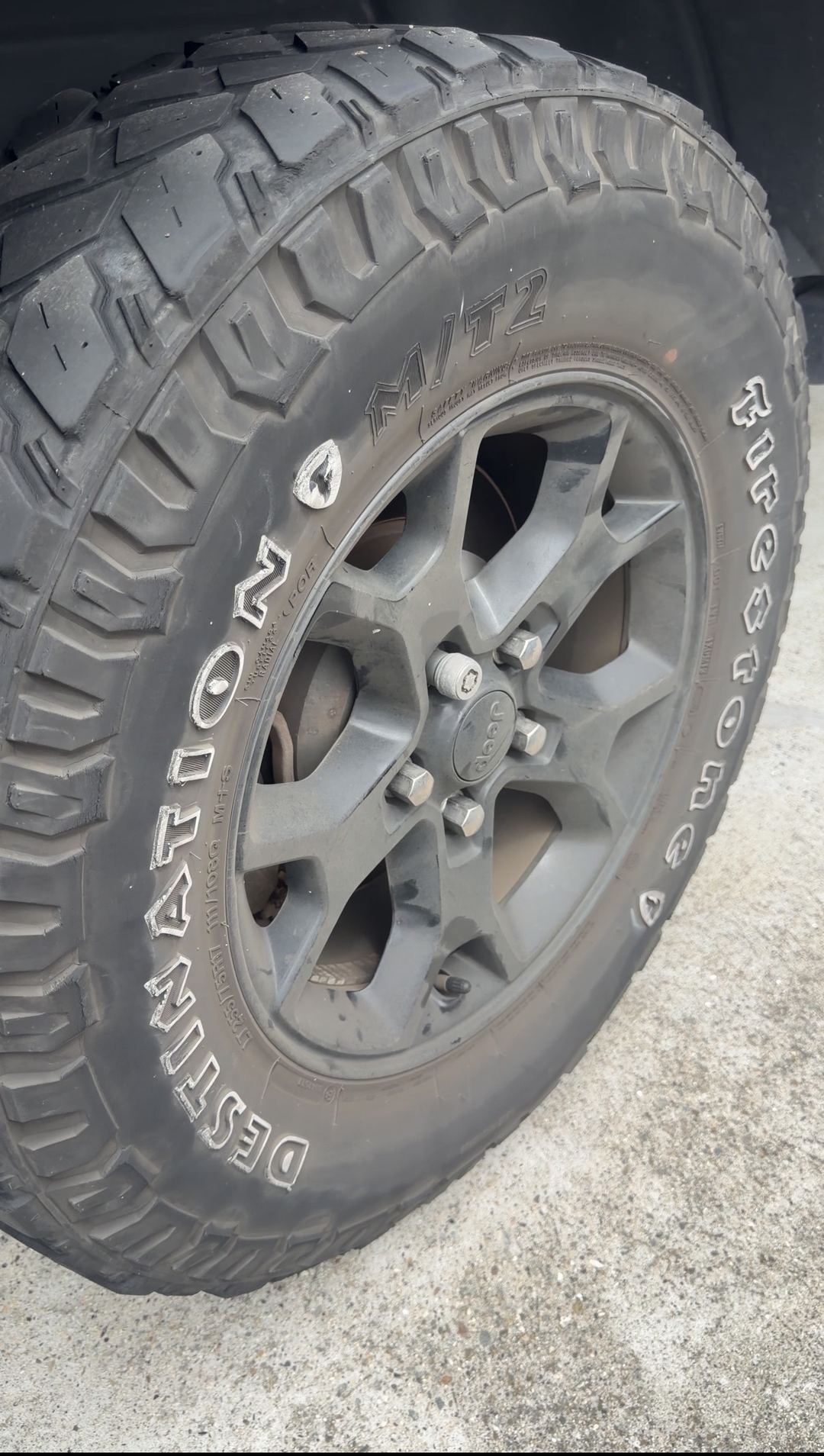 Dusty Firestone Destination M/T2 tyre and grey-looking wheel on a Jeep Wrangler before cleaning