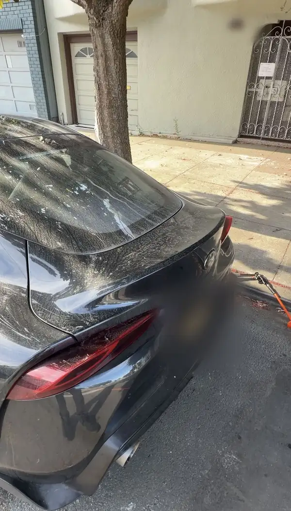 Rear of a black Toyota GR Supra before detailing, its decklid and rear glass covered in dried water spots and dirt.