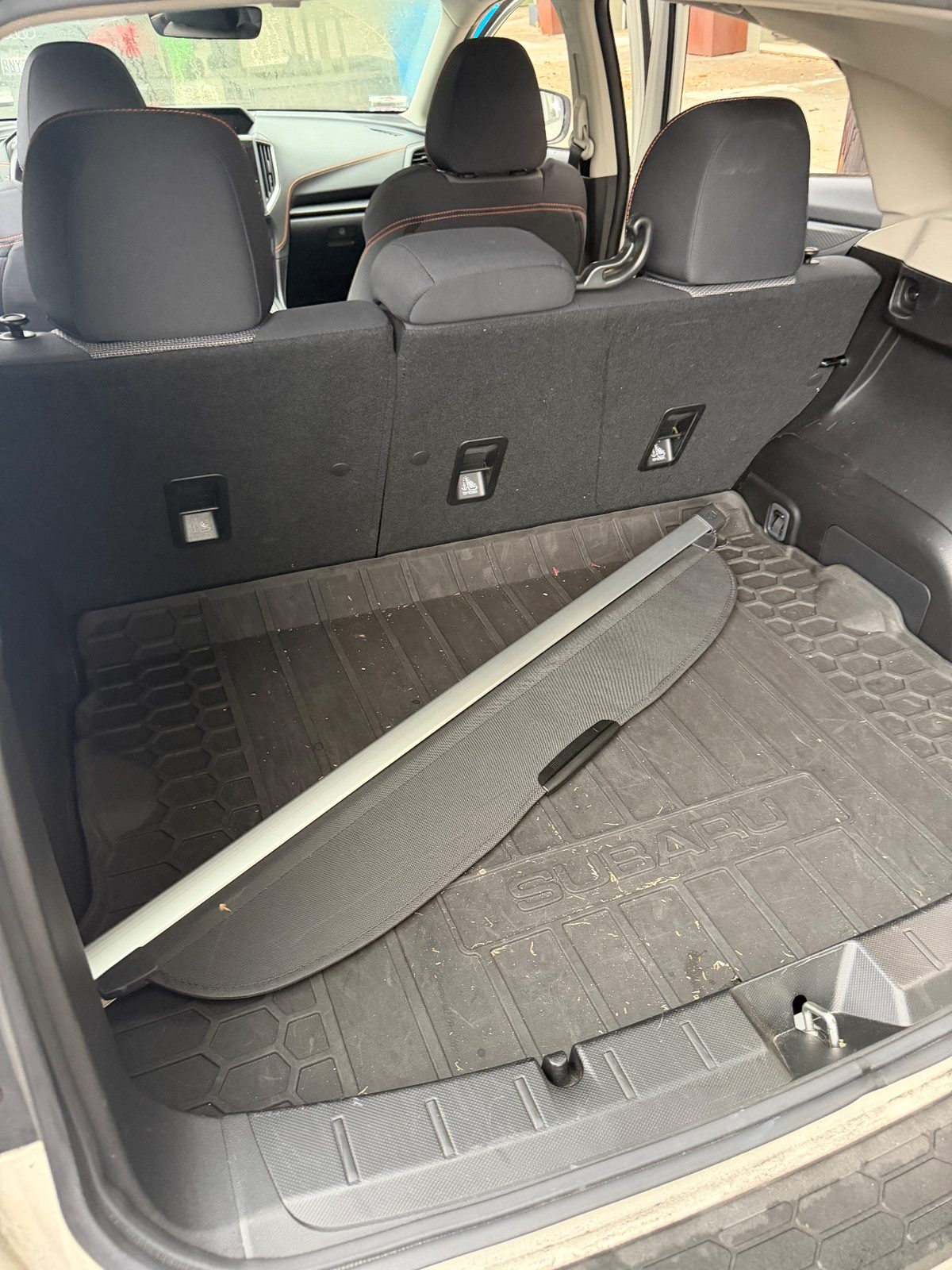 Cargo area of a Subaru Crosstrek before cleaning, leaves and crumbs on the rubber liner