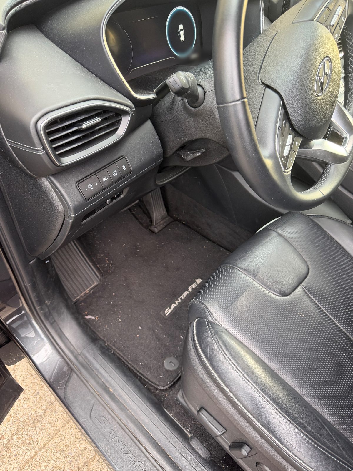 Driver footwell of a dark grey Hyundai Santa Fe before detailing, with crumbs and grit on the carpet mat