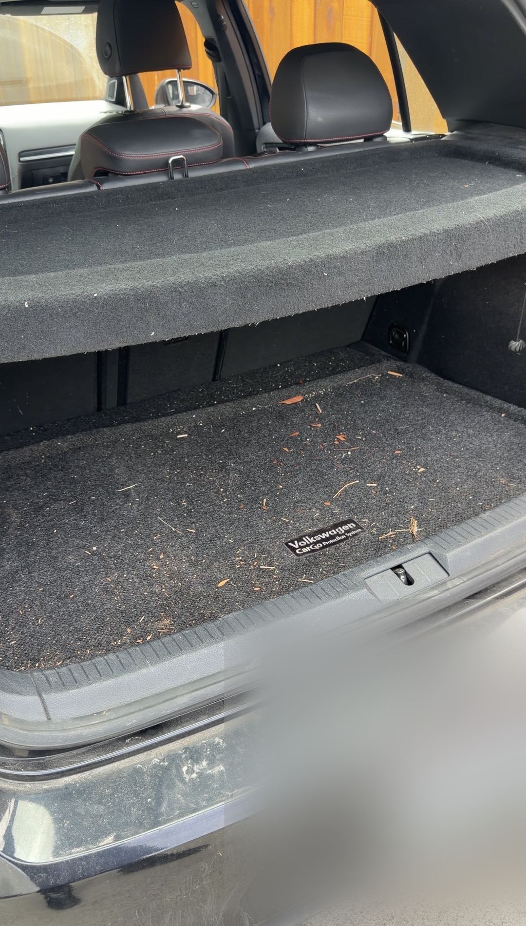 Trunk of a black VW GTI before cleaning, carpet covered in wood chips and debris