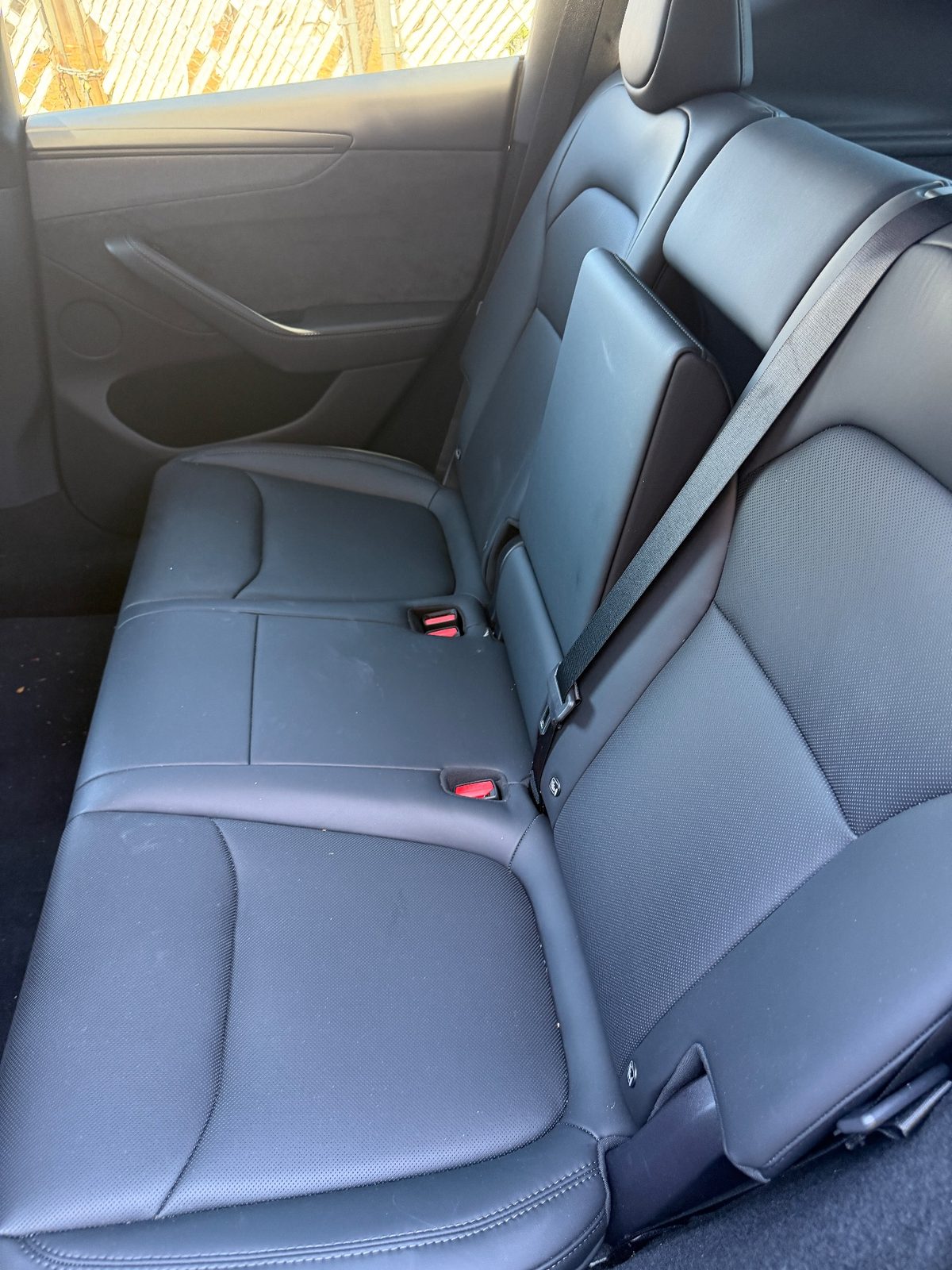 Rear seat of a white Tesla Model Y before cleaning, dusty leather and debris on the carpet