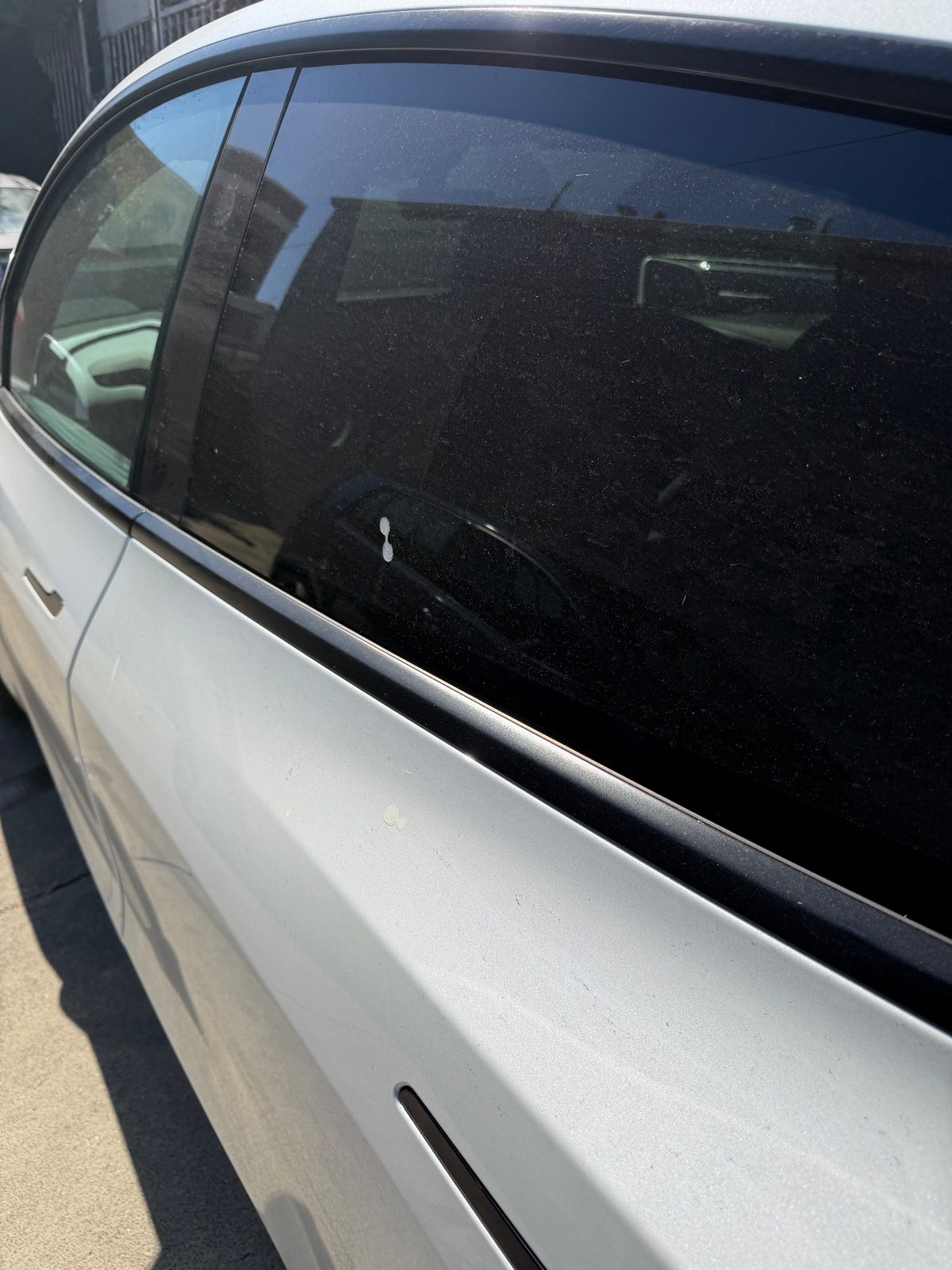 Rear door and window of a white Tesla Model Y before washing, speckled dusty glass