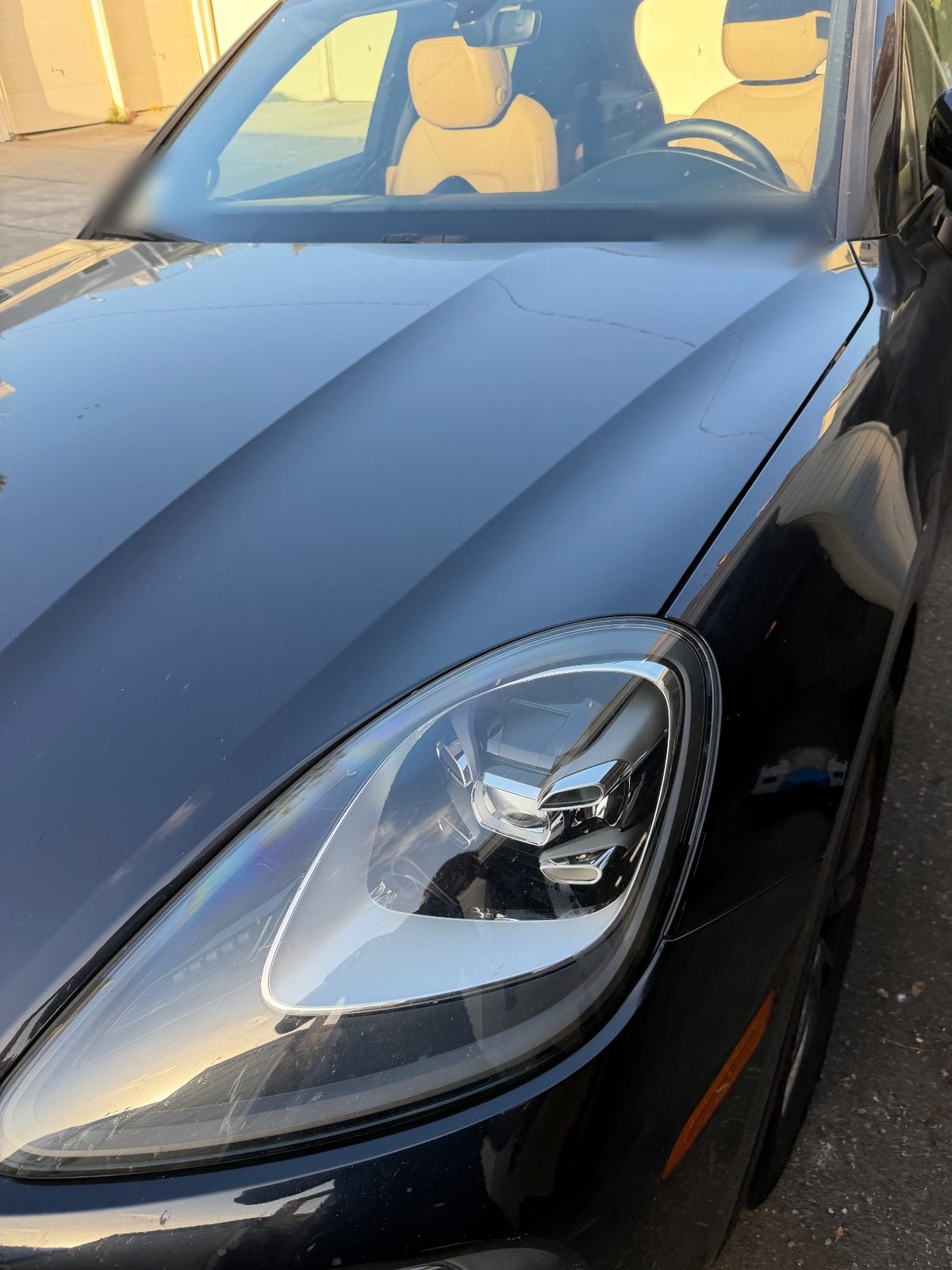 Hood and headlight of a dark blue Porsche Cayenne before washing, dust film and hairline cracks in the paint