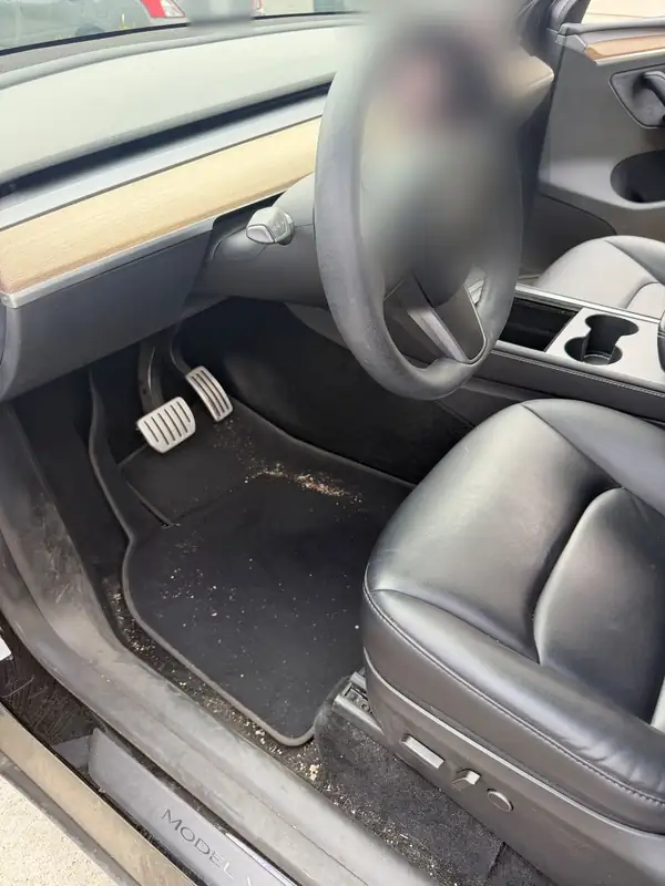 Driver seat and footwell of a black Tesla Model Y before detailing, with sand on the floor mat