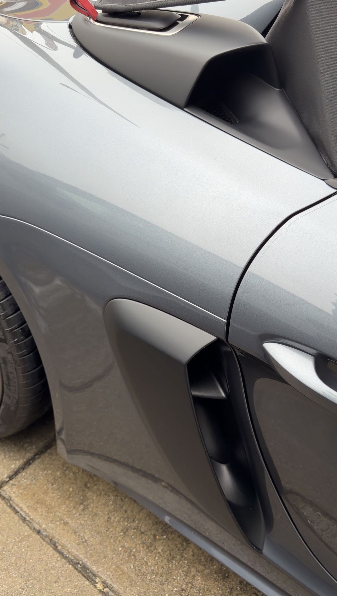 The black side air intake and rear quarter panel of a clean grey Porsche 718 Spyder RS.