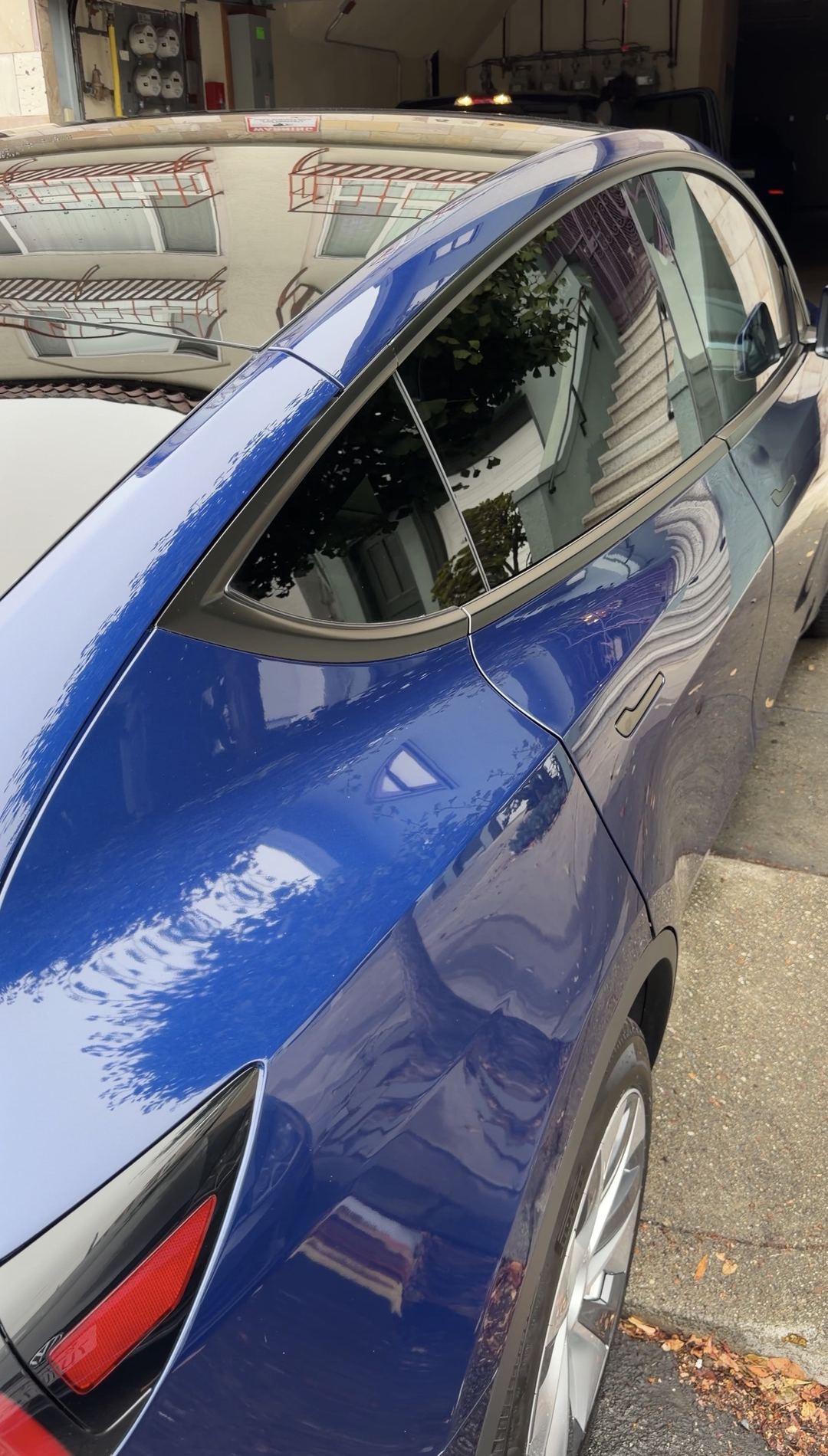 Clean rear door and quarter panel of a deep blue Tesla Model Y reflecting a building after detailing.